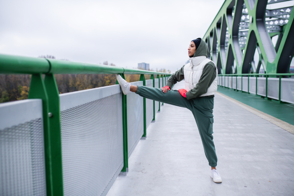 Young muslim woman doing stretching before morning jogging in a city.