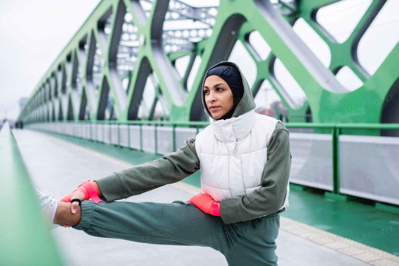 Young muslim woman doing stretching before morning jogging in a city.