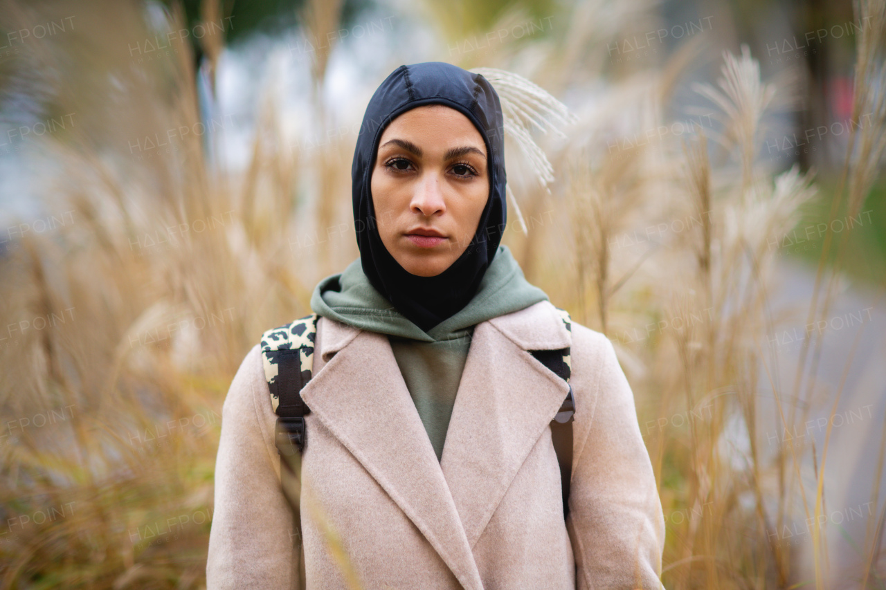 Portrait of young muslim woman in coat, standing outdoor in a city park.