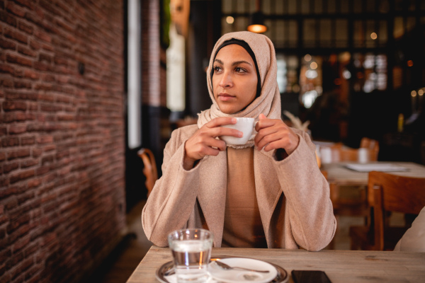 Young muslim woman enjoying cup of coffe in a cafe.