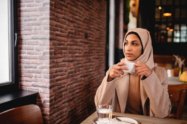 Young muslim woman enjoying cup of coffe in a cafe.