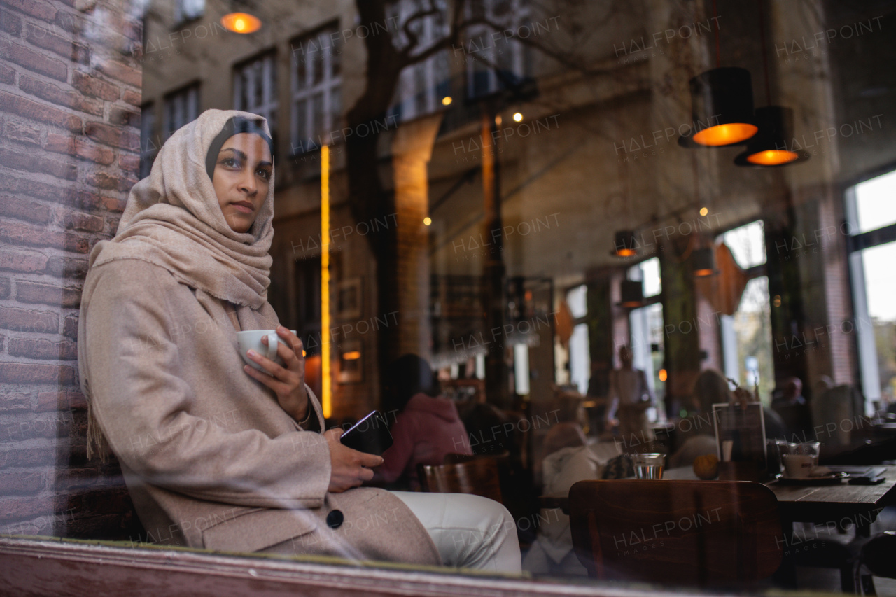 Young muslim woman with smartphone enjoying cup of coffe in a cafe.