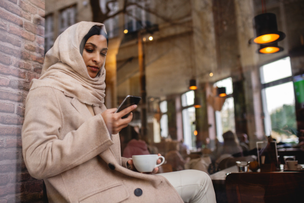 Young muslim woman with smartphone enjoying cup of coffe in a cafe.