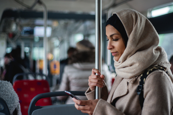 Young muslim woman with a smartphone in public bus.