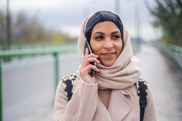 Portrait of young muslim woman walking and calling in city.