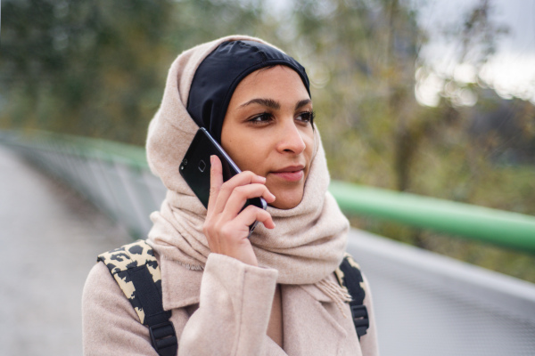 Portrait of young muslim woman walking and calling in city.