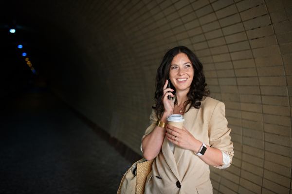 A successful happy businesswoman commuting in the morning in city street, calling on mobile phone and holding cofee cup.