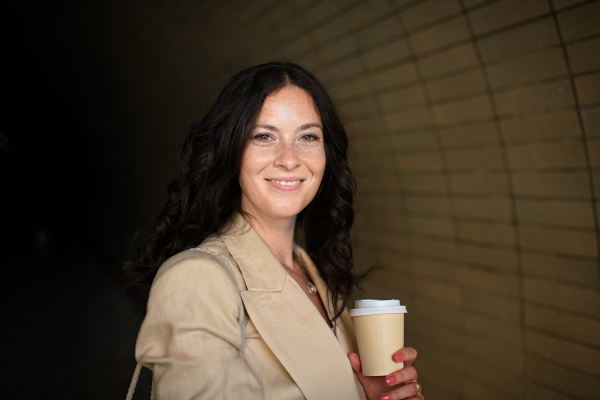 A successful happy businesswoman commuting in the morning in city street, holding cofee cup.