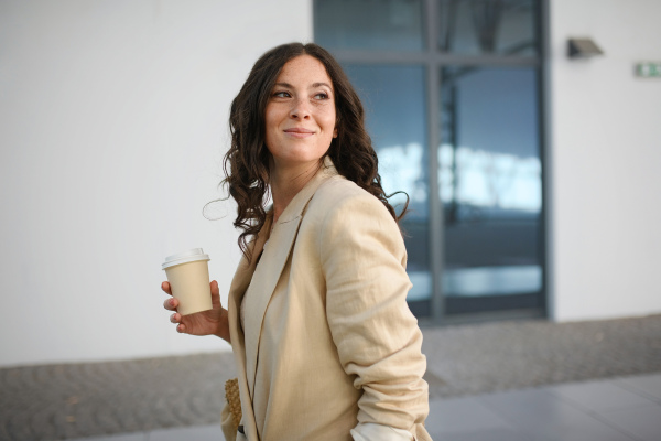 A successful happy businesswoman commuting in the morning in city street, holding cofee cup.