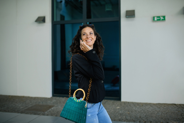 A successful happy businesswoman commuting in the morning in city street, calling on mobile phone.