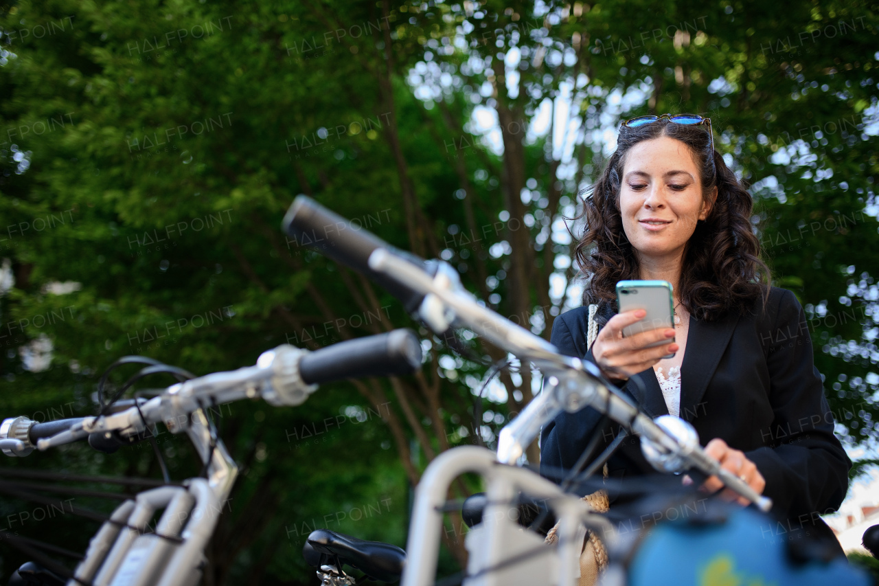 A businesswoman with bike sitting and using smartphone. Commuting and alternative transport concept