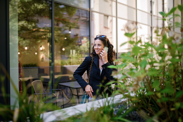 A happy woman calling on mobile phone and waiting outside the cafe in city.