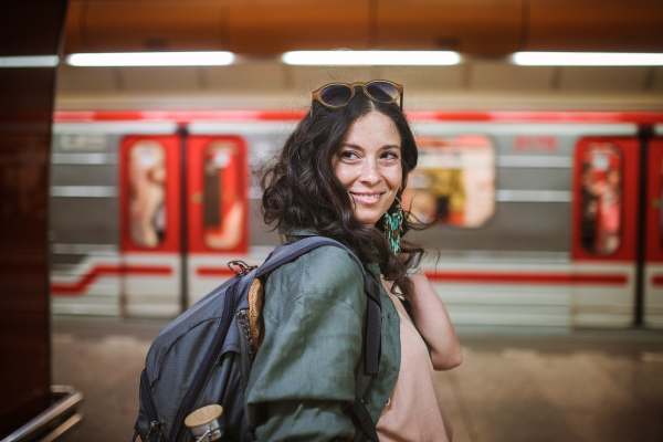 Mid adult woman commuter is standing in a subway station and looking at camera.