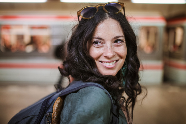 Mid adult woman commuter is standing in a subway station and looking at camera.