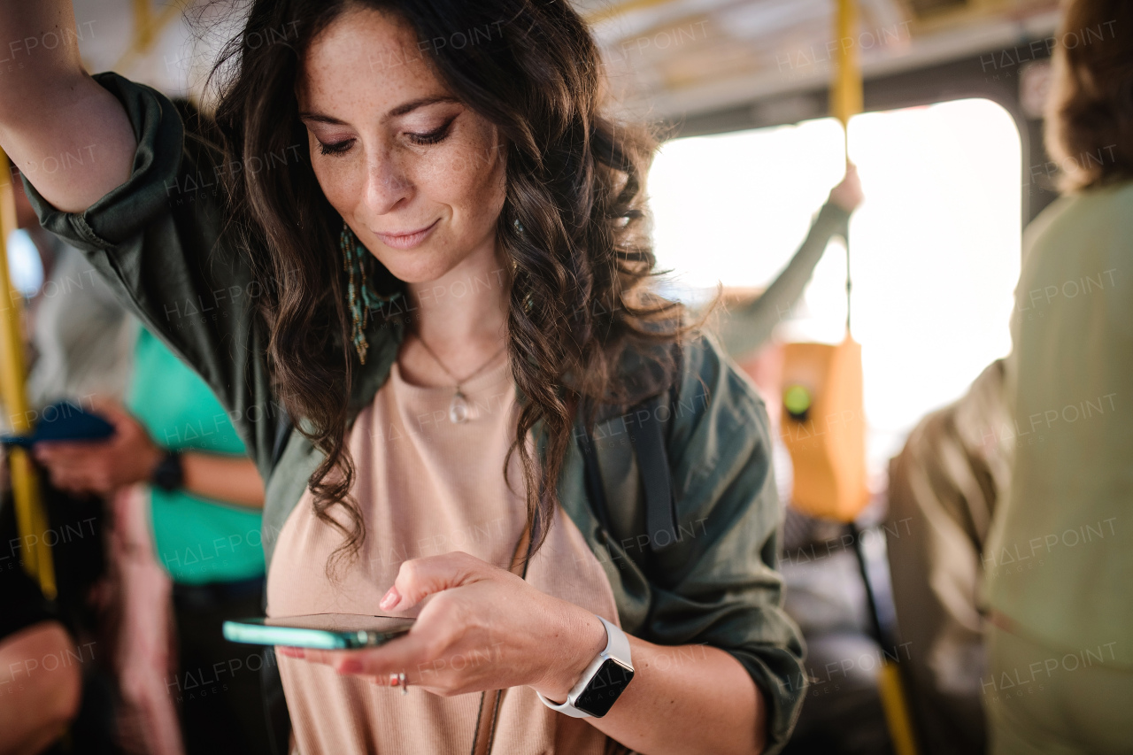 A mid adult woman commuter is standing in bus and using the phone.