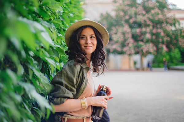 A woman candid portrait from park. Young urban female tourist with water bottle smiling.