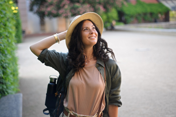 A young beautiful female traveler with backpack walking through bridge on sunny day in city.