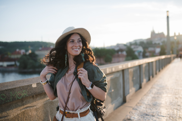 A young beautiful female traveler with backpack walking through bridge on sunny day in city.