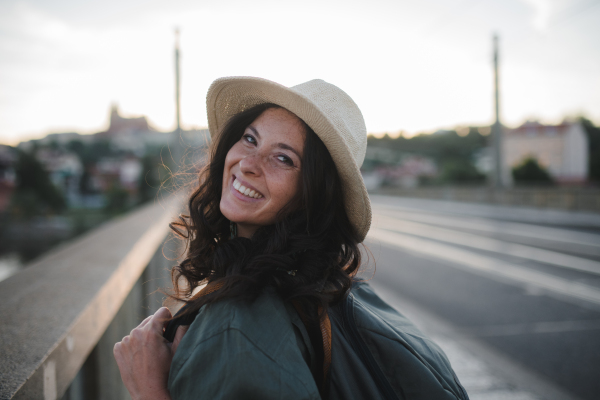 A young beautiful female traveler with backpack walking through bridge on sunny day in city.