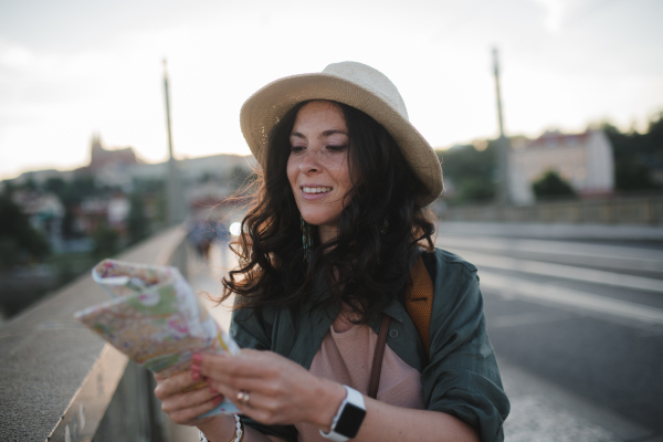 A young beautiful female traveler with backpack and map walking through bridge on sunny day in city.