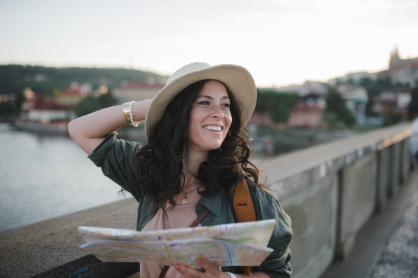 A young beautiful female traveler with backpack and map walking through bridge on sunny day in city.