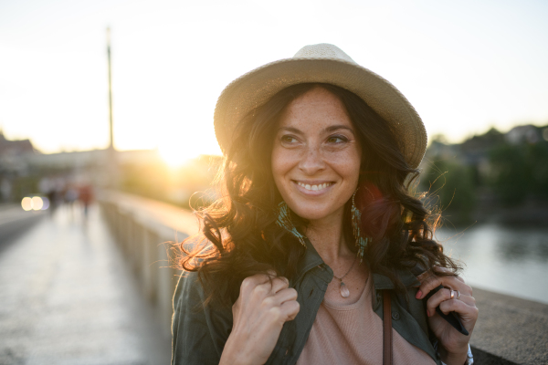 A young beautiful female traveler with backpack walking through bridge on sunny day in city.