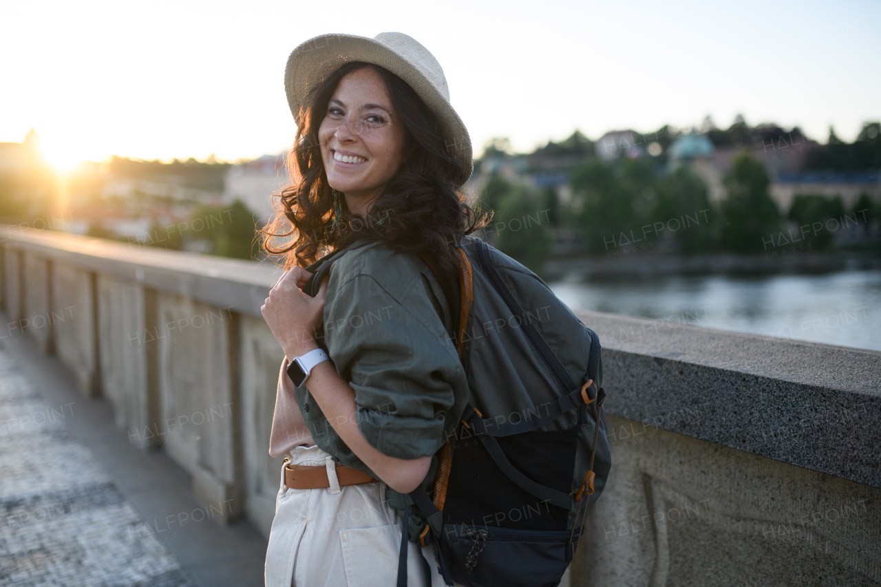 A young beautiful female traveler with backpack walking through bridge on sunny day in city.