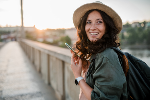 A young beautiful female traveler with backpack walking through bridge on sunny day in city.