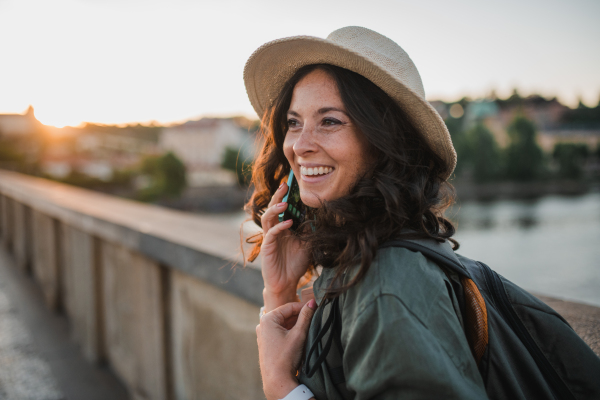 A young beautiful female traveler with backpack walking through bridge on sunny day in city.