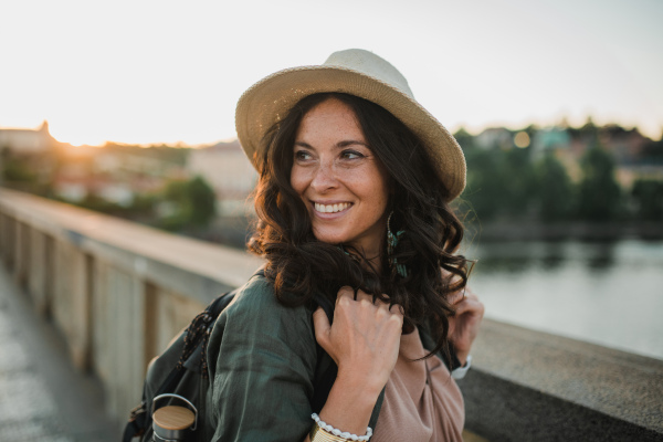 A young beautiful female traveler with backpack walking through bridge on sunny day in city.