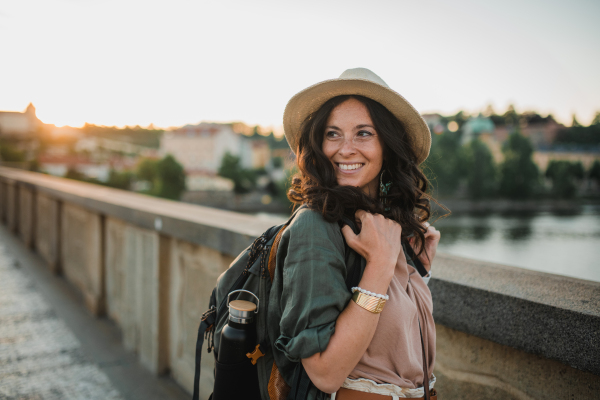 A young beautiful female traveler with backpack walking through bridge on sunny day in city.