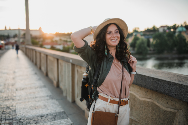 A young beautiful female traveler with backpack walking through bridge on sunny day in city.