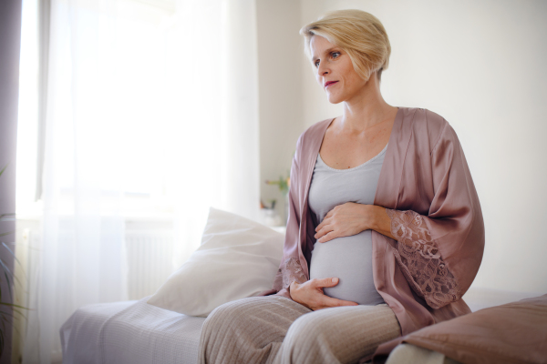 Happy pregnant woman stroking her belly sitting on a bed.