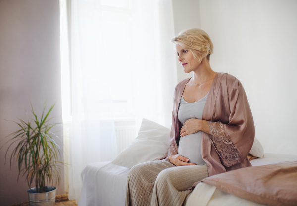 Happy pregnant woman stroking her belly sitting on a bed.