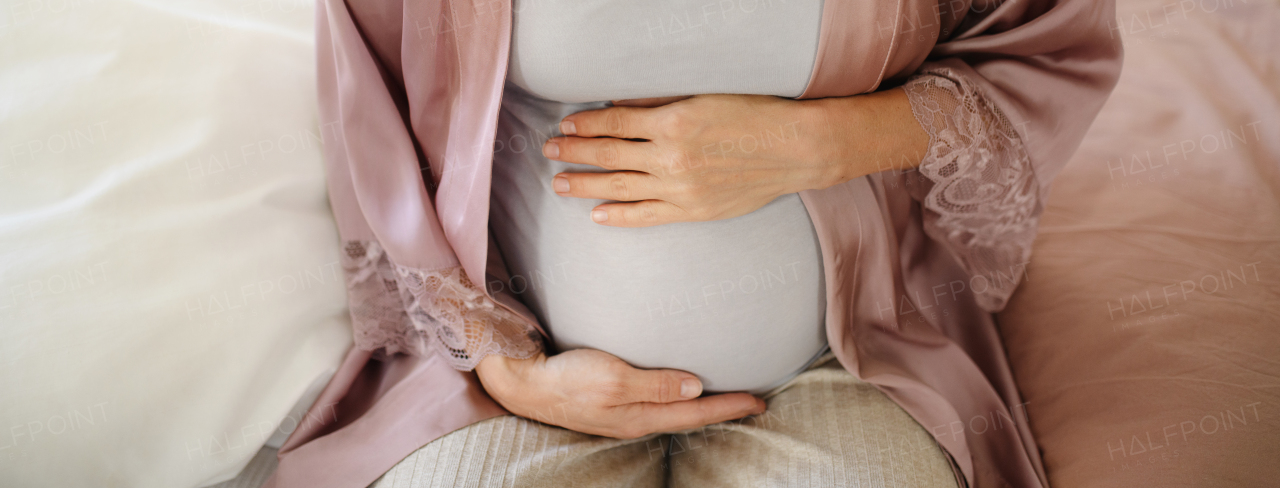 Close-upof pregnant woman stroking her belly sitting on a bed.