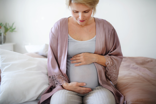 Happy pregnant woman stroking her belly sitting on a bed.