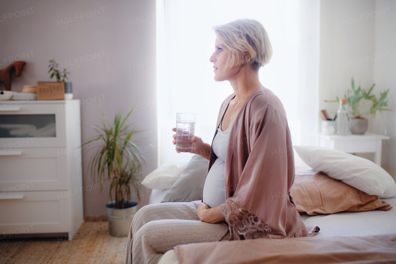 Pregnant woman drinking water in a bed, at morning. Healthy lifestyle and morning routine in pregnancy, concpet.