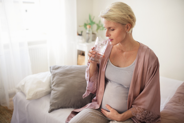 Pregnant woman drinking in a bed, at morning. Healthy lifestyle and morning routine in pregnancy, concpet.