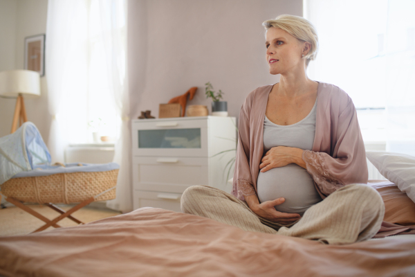 Happy pregnant woman stroking her belly sitting on a bed.