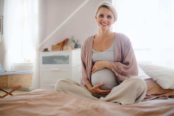 Happy pregnant woman stroking her belly sitting on a bed.