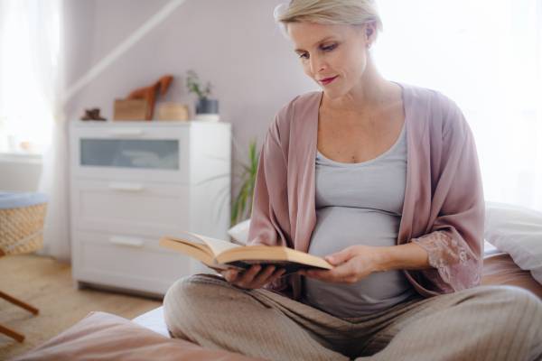 Pregnant woman sitting on bed and reading a book.