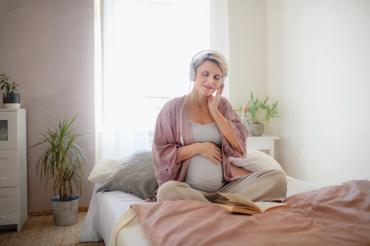 Pregnant woman sitting in a bed, listening music and reading book, enjoying time for herself.