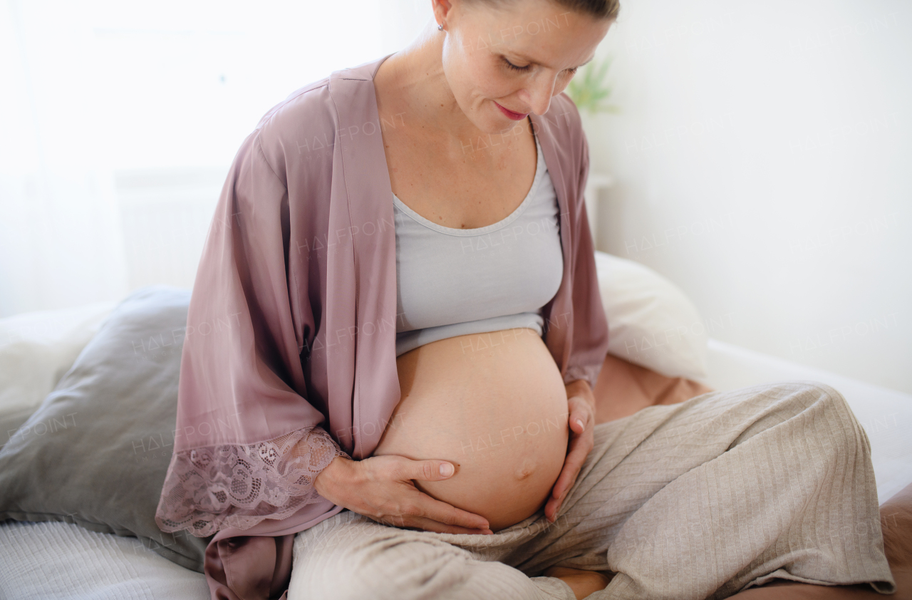 Happy pregnant woman stroking her belly sitting on a bed.