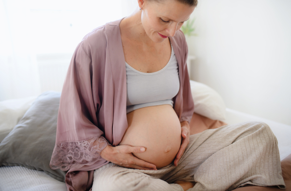 Happy pregnant woman stroking her belly sitting on a bed.