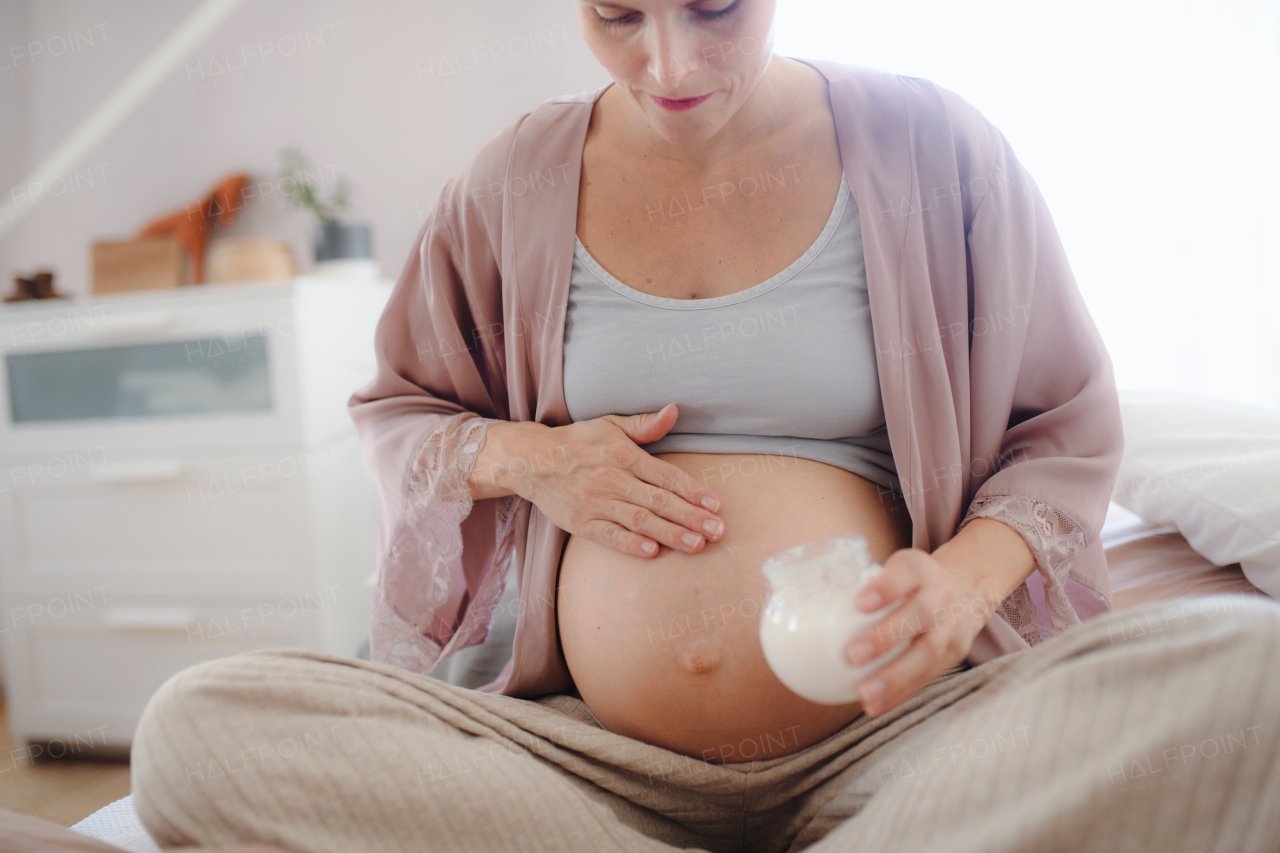 Pregnant woman creaming her belly,sitting in a bed, taking care of herself.