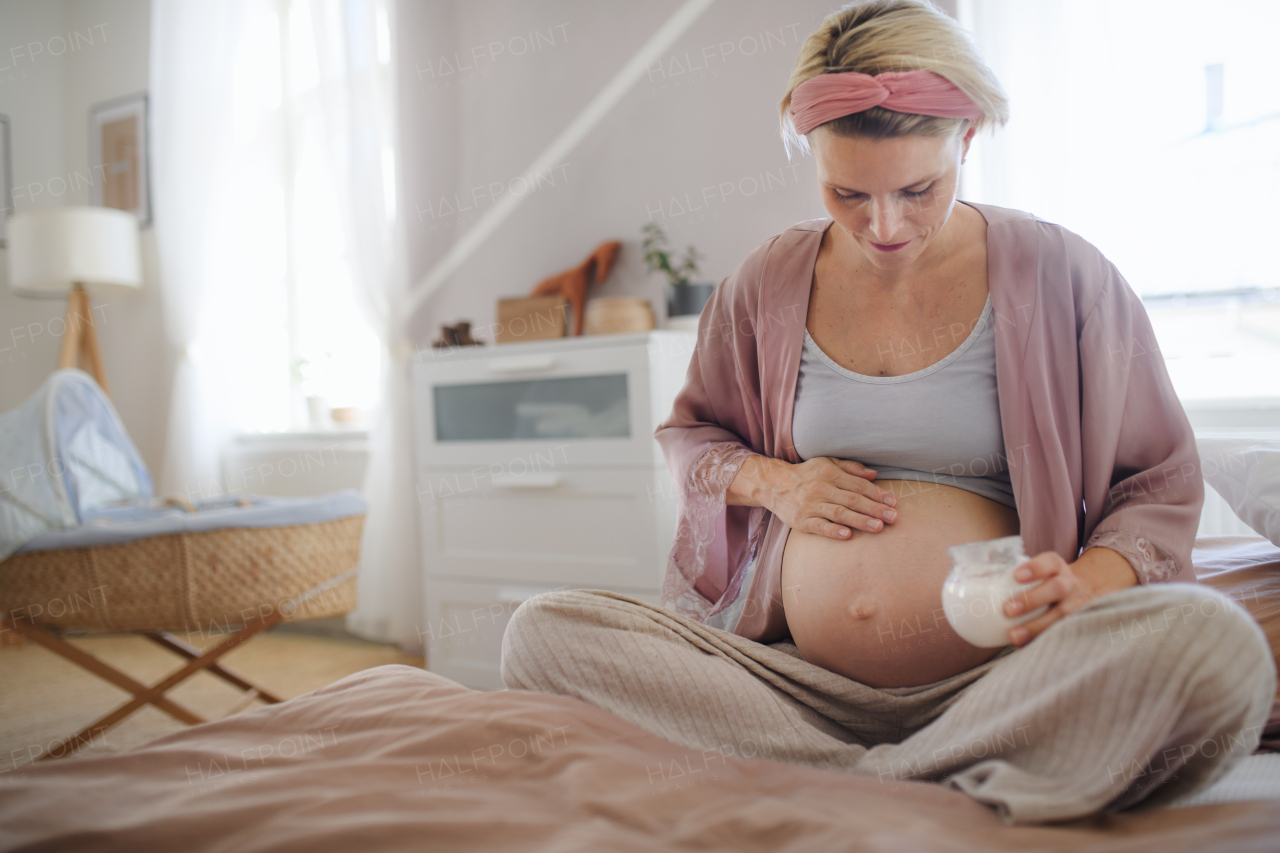 Pregnant woman creaming her belly,sitting in a bed, taking care of herself.