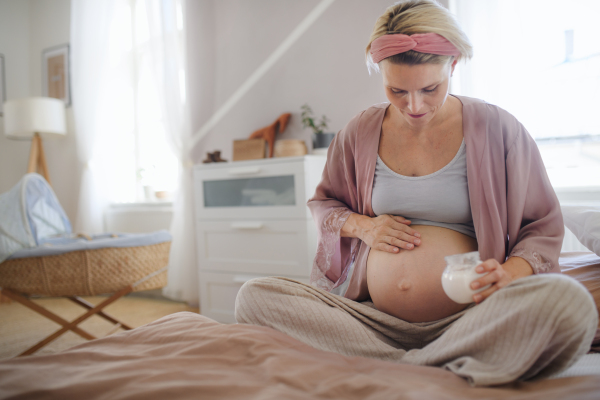 Pregnant woman creaming her belly,sitting in a bed, taking care of herself.