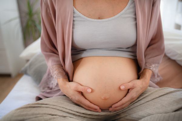 Happy pregnant woman stroking her belly sitting on a bed.