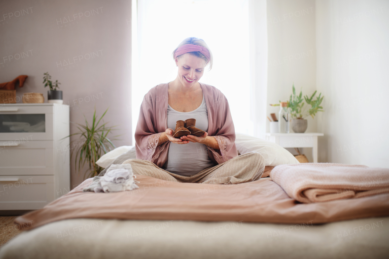 Happy pregnant woman holding a little shoes for her baby.