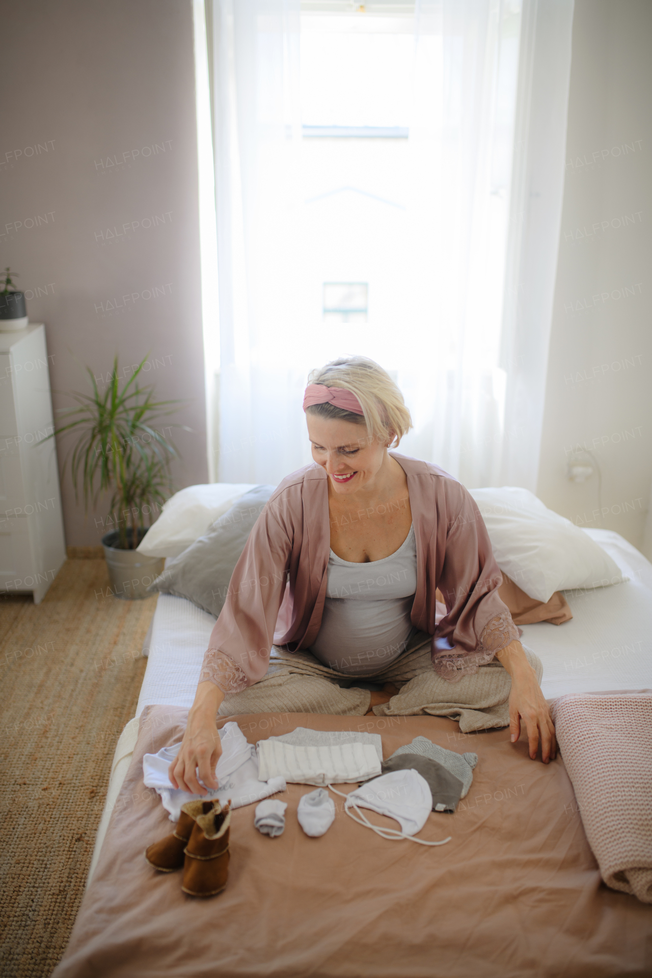 High angle view of pregnant woman looking at little clothes for baby, packing them to maternity ward.